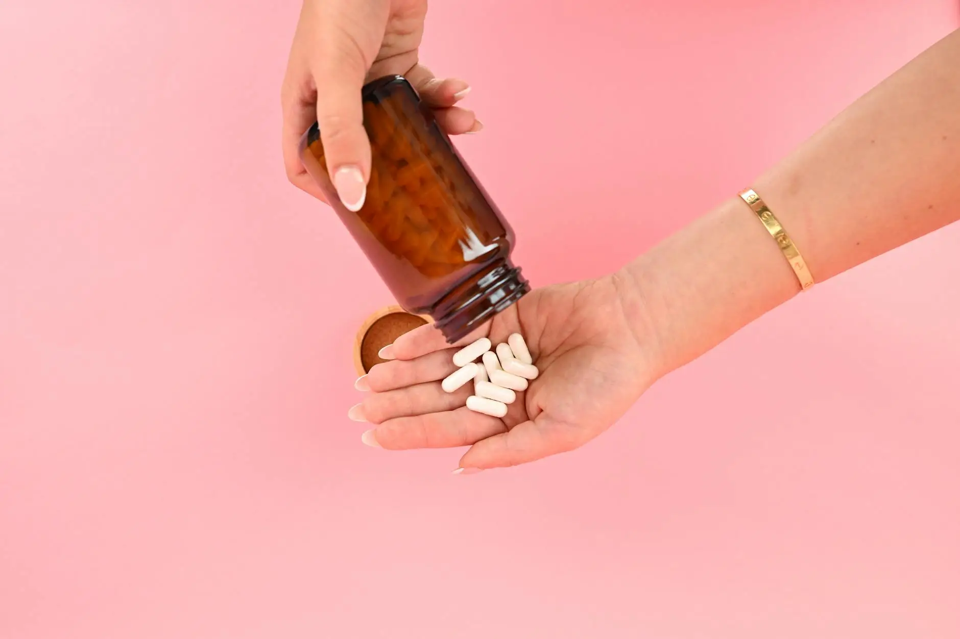 hands pouring capsules from brown bottle on pink background pcos supplements pcos routine pcos self-care