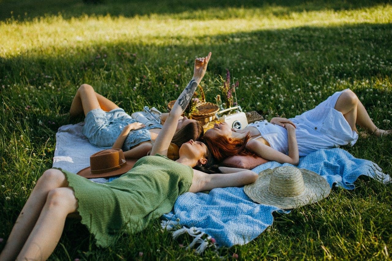 Group of friends relaxing on blankets in a sunny meadow with a picnic basket nearby.